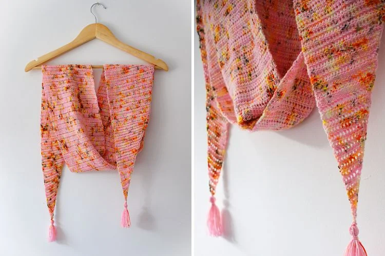 Handmade tasseled shawl hanging on a wooden hanger against a white wall.