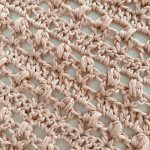 Close-up of a light pink crocheted lace fabric with an open, textured pattern, reminiscent of the Vintage Tulip Shawl. 