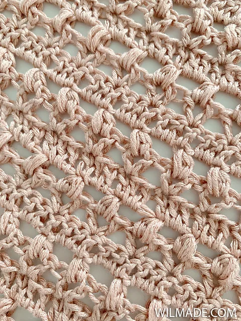 Close-up of a light pink crocheted lace fabric with an open, textured pattern, reminiscent of the Vintage Tulip Shawl. 