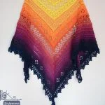 The Flower Valley Shawl is a crochet shawl with a gradient of yellow, orange, pink, and navy blue.