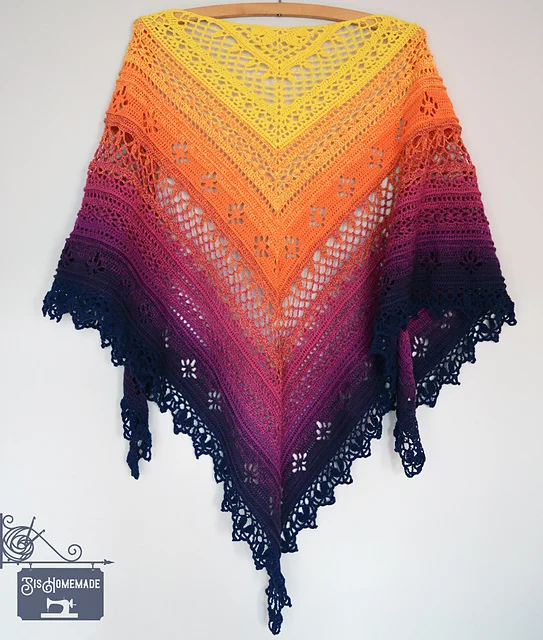 The Flower Valley Shawl is a crochet shawl with a gradient of yellow, orange, pink, and navy blue.