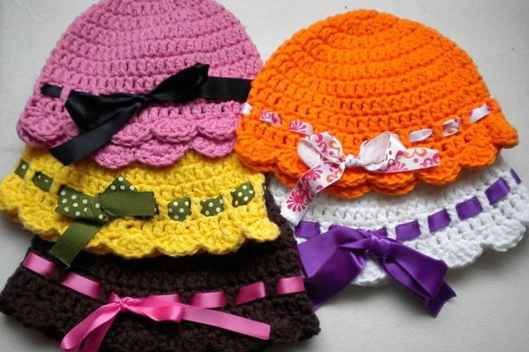 a set of crochet baby hats in different colors adorned with ribbons