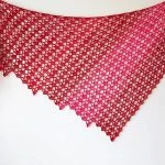 The Hot Chili Shawl, a pink, triangular lace shawl with an openwork crochet pattern, is displayed against a white background.