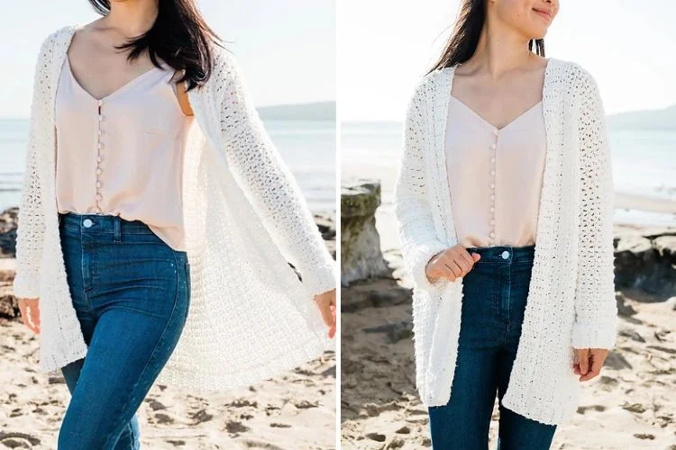 A woman wearing a white blouse, blue jeans, and a white cardigan, standing on a beach with sunlight illuminating her from behind.