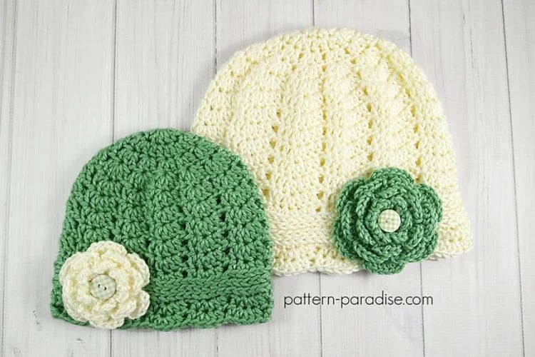 two crochet baby hats in greena and white adorned with a crochet flower