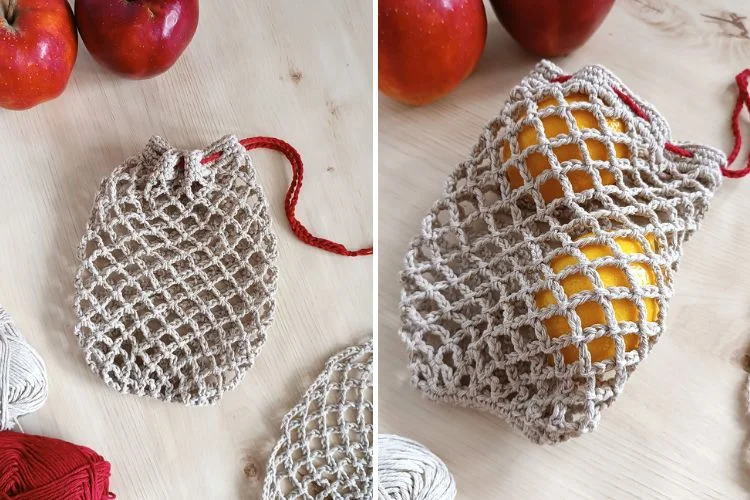 A beige crocheted mesh bag filled with apples on a wooden surface next to yarn balls.