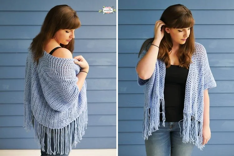 A woman with long brown hair wearing a black top and blue crocheted shawl with fringe, standing against a blue wooden background.