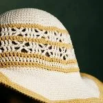 A close-up of the Shangri-la Sunhat, featuring white and yellow stripes with decorative patterns, set against a dark green background.