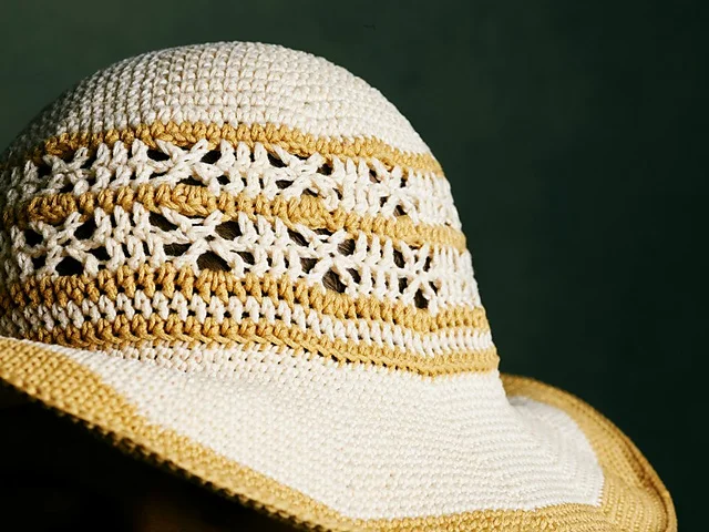 A close-up of the Shangri-la Sunhat, featuring white and yellow stripes with decorative patterns, set against a dark green background.