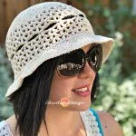A woman wearing large sunglasses and a stylish Lunette Sun Hat outdoors, with greenery softly blurred in the background.