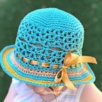 A child wearing a blue, brown, and yellow Lunette Sun Hat with a decorative yellow ribbon bow, photographed from above.