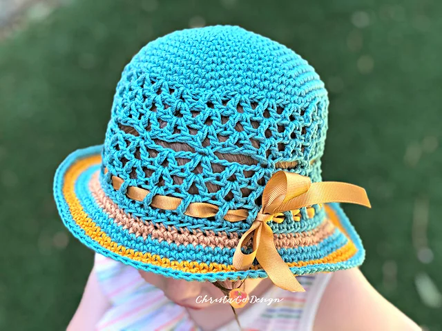 A child wearing a blue, brown, and yellow Lunette Sun Hat with a decorative yellow ribbon bow, photographed from above.