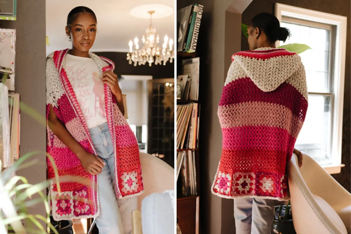 In a cozy room adorned with a chandelier, a person stands wearing an Auto Draft-designed crochet hooded vest featuring colorful stripes of pink, red, and cream.