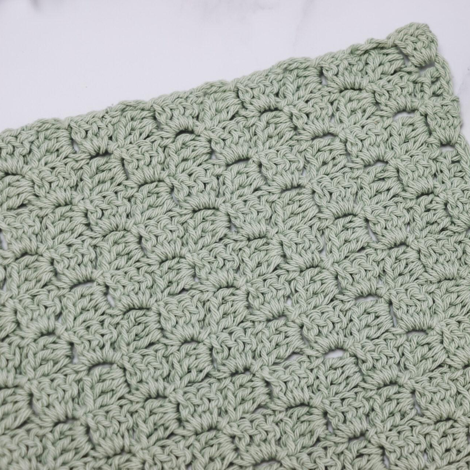 A close-up of a light green crocheted fabric with a textured, scalloped pattern.