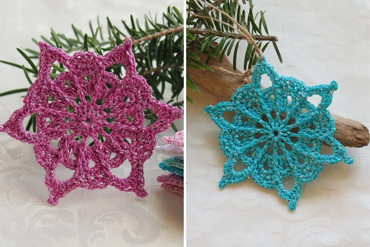 Two crochet snowflakes—one pink, one blue—delicately crafted like frosted lace, are displayed on a light surface with a pine branch in the background.