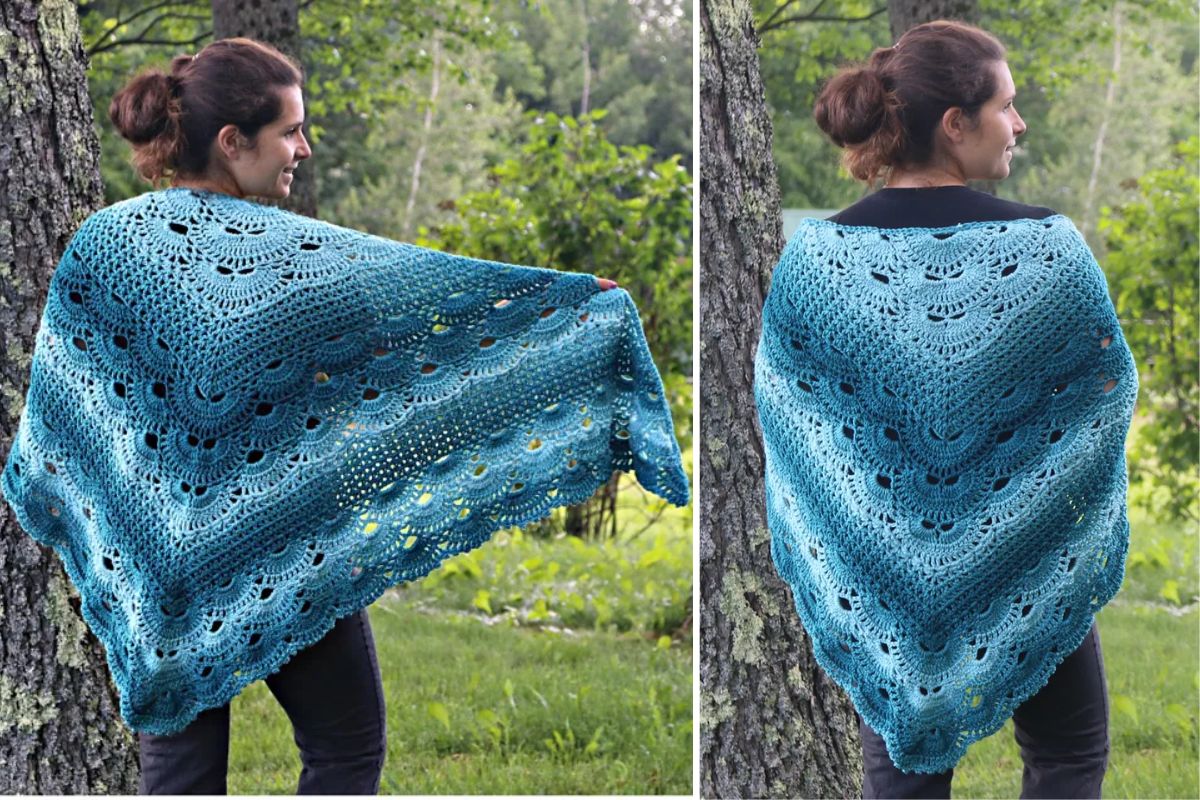 A person outdoors elegantly dons Victoria's German Shells Shawl in a blue crocheted lace pattern, showcasing it draped gracefully over their shoulders and fanned out behind them.