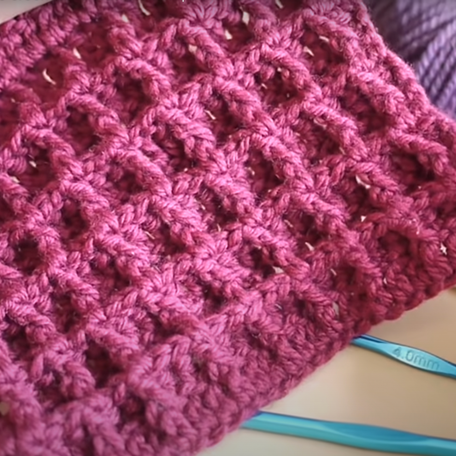 A section of purple crochet fabric with a textured pattern is shown alongside blue crochet hooks.