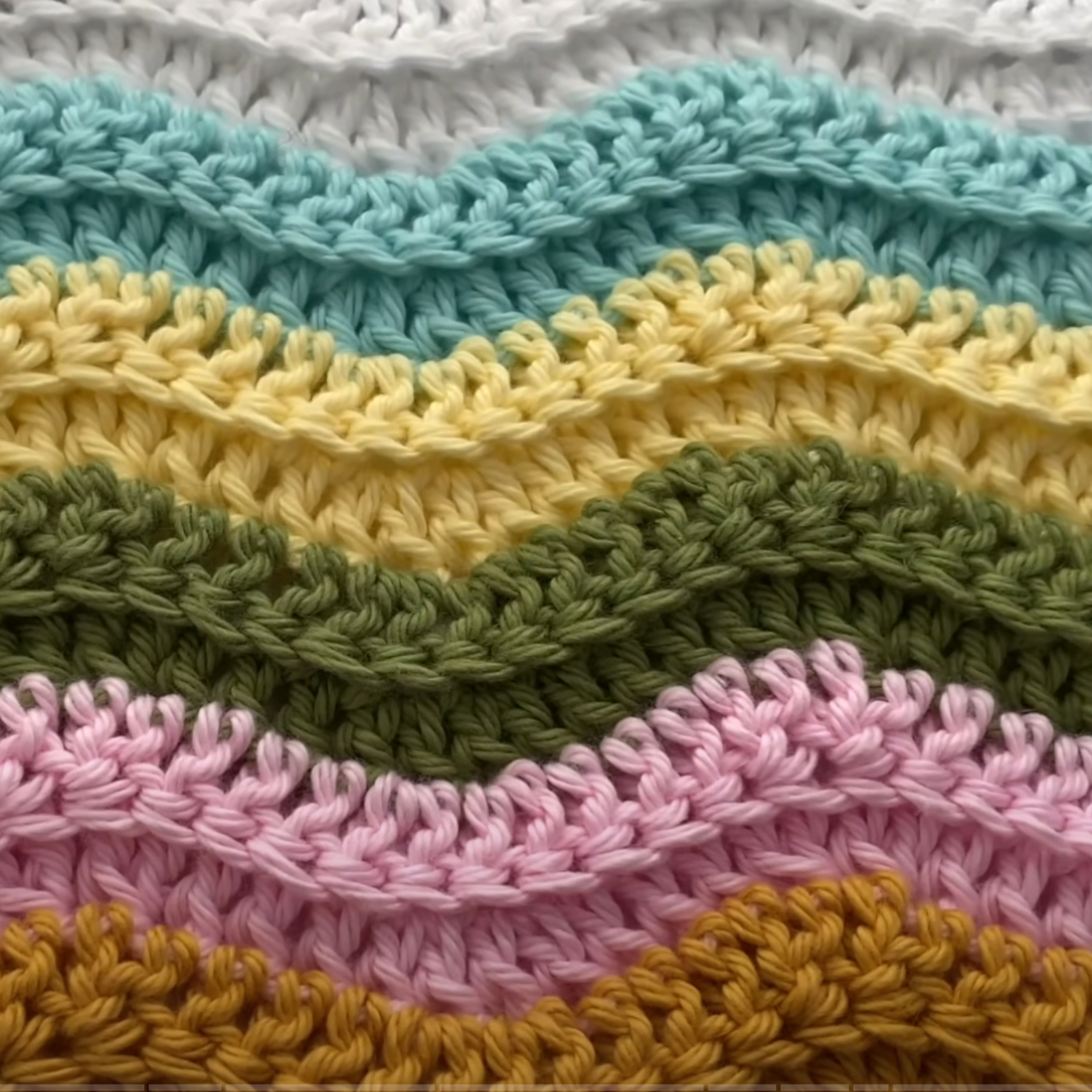 Close-up of a crocheted zigzag pattern with rows of white, light blue, yellow, green, pink, and mustard yarn.