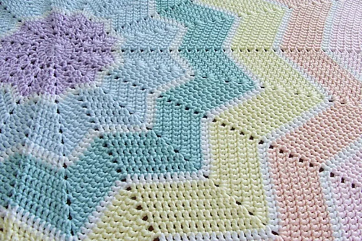 Close-up of a crocheted blanket with zigzag pattern in pastel colors, including shades of purple, green, yellow, and peach.