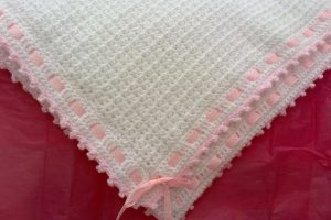 a white crochet baby blanket with a pink ribbon border