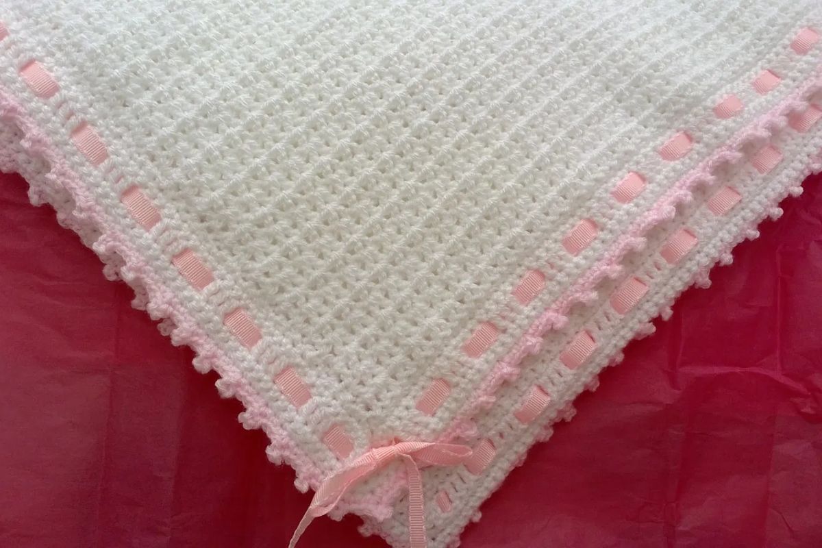 a white crochet baby blanket with a pink ribbon border