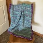 a crochet baby blanket worked with variegated yarn featuring a purple frilly border