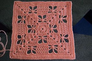 a pink crochet square with lace butterfly motifs