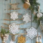 Wall display featuring a tree shape made of sticks and string, decorated with crocheted snowflakes, Winter Flower ornaments, and festive greenery, with small figurines and a shimmering Flower Star bauble at the base.