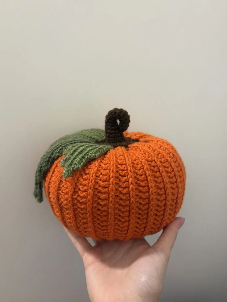 hand holding an orange crochet pumpkin