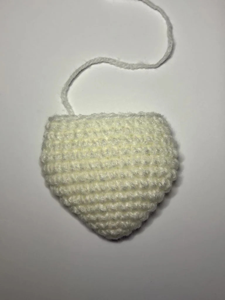 A small, white, crocheted half-oval shape with a yarn tail attached, placed on a plain white background—perfect for your next crochet pumpkin pattern project.