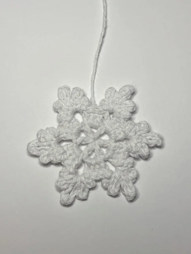 A white crocheted snowflake ornament with six points and a loop of yarn at the top, displayed on a plain white background—a charming addition to your holiday decor or your next pumpkin crochet pattern project.