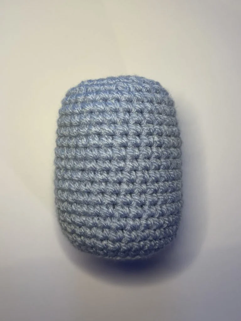 A small, light blue, crocheted cylindrical object—perfect as a whimsical crochet gnome body—is displayed on a plain white background.