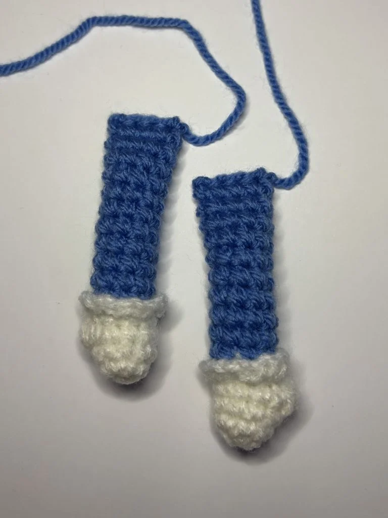 Two crocheted blue and white objects with attached blue yarn, crafted in a pumpkin crochet pattern, are placed on a plain white surface.