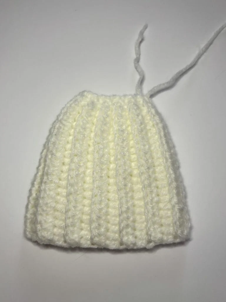 A small, hand-crocheted white piece of fabric with vertical ribbing and two loose yarn ends—perfect for starting your next pumpkin crochet pattern or free crochet pumpkin pattern project. Shown against a plain background.