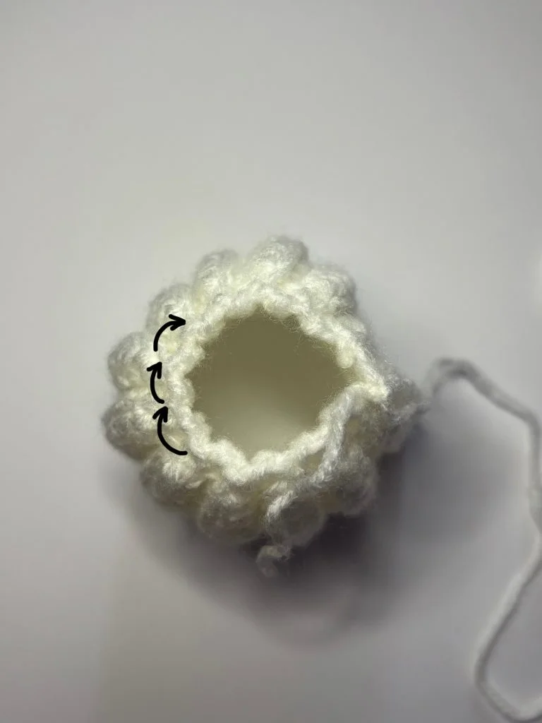 White crocheted piece in a round shape with a hole in the center, featuring a black arrow drawn on the yarn to show the direction of stitching—perfect for starting your next crochet pumpkin pattern free project.