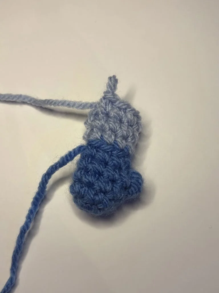 A small crochet piece with a blue bottom and light gray top, placed on a white surface, inspired by a pumpkin crochet pattern.
