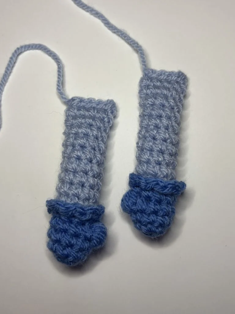 Two crocheted objects in light blue yarn with darker blue, scalloped ends and attached strands rest on a white surface—perfect accents for your next pumpkin crochet pattern project.