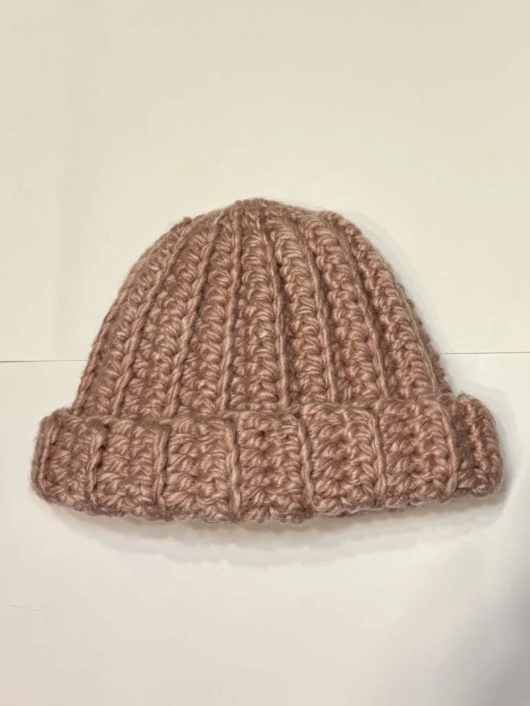 A crocheted, chunky ribbed beanie hat in a light brown color is displayed on a plain white background alongside a matching crochet headband.