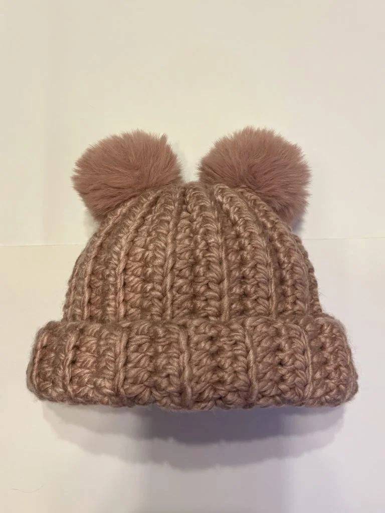 A crochet brown beanie hat with two large, fluffy pom-poms on top, displayed on a plain white background—perfect for pairing with your favorite crochet headband.