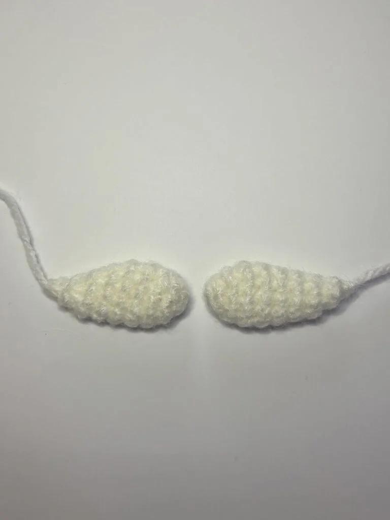 Two small, crocheted, off-white oval shapes with yarn tails are placed side by side on a white surface, perfect as the start of a pumpkin crochet pattern.