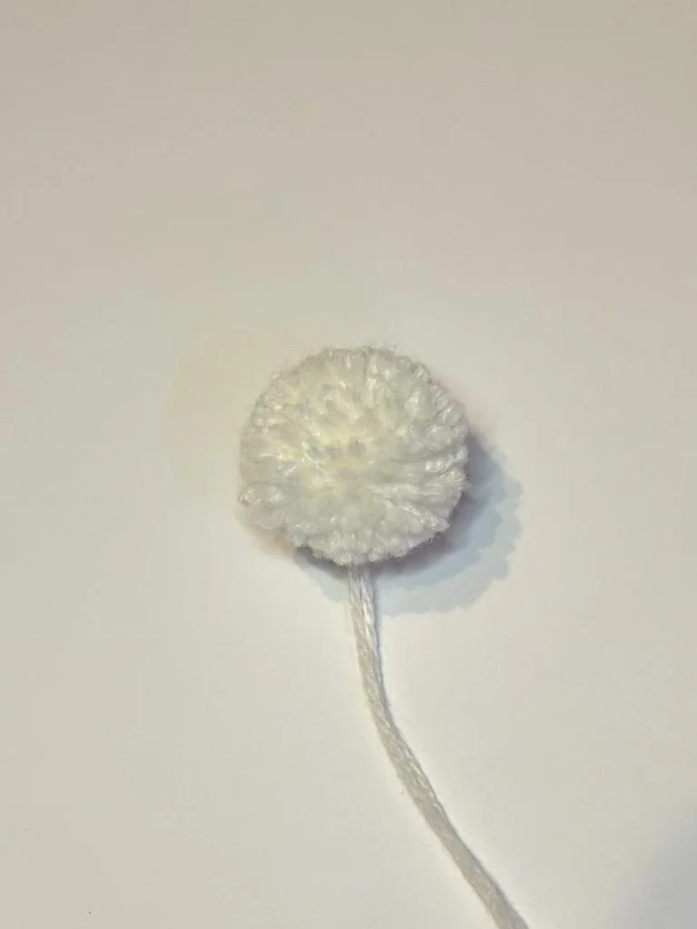 A small, round, white crocheted piece with a yarn tail is placed on a plain light background, perfect as the start of a cute crochet pumpkin pattern.