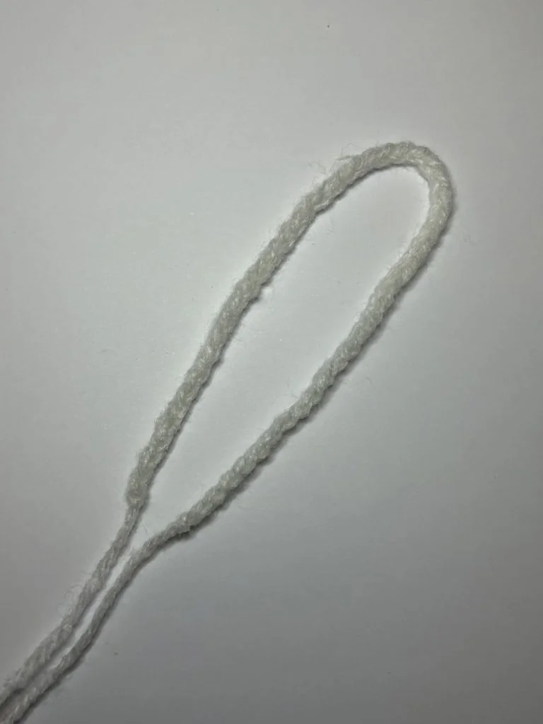 A piece of white yarn is arranged in a simple loop on a plain white background, ready to be transformed into a charming creation using a free crochet pumpkin pattern.