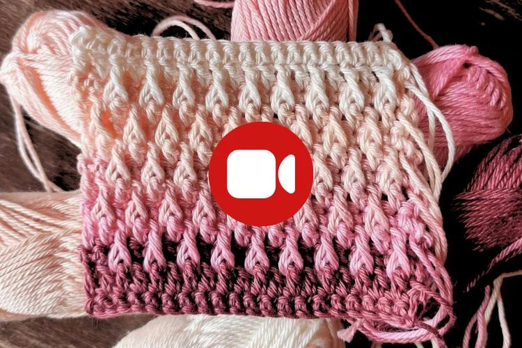 A rectangular swatch of pink and white gradient crochet with yarn skeins in the background; a video camera icon is centered on the crochet.