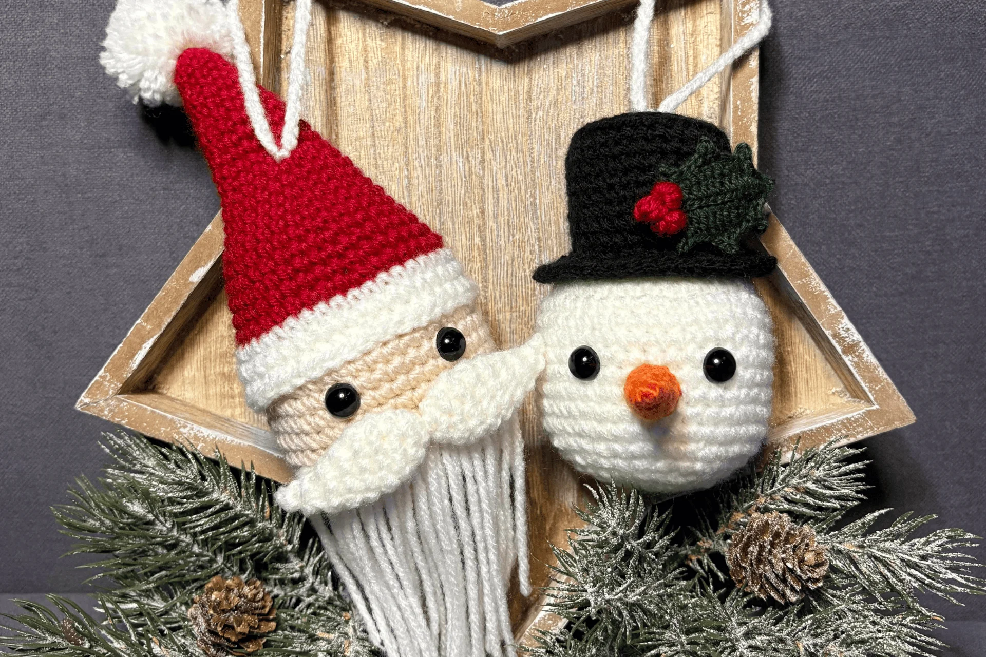 Crocheted Santa Claus and snowman ornaments hang on a wooden star frame decorated with pine branches, pine cones, and a charming pumpkin crochet pattern for added festive flair.