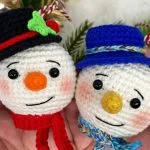 Two crocheted Snowman Ornaments by Cuddly Stitches Craft are held in hands; one features a red hat and scarf, the other a blue hat and scarf.