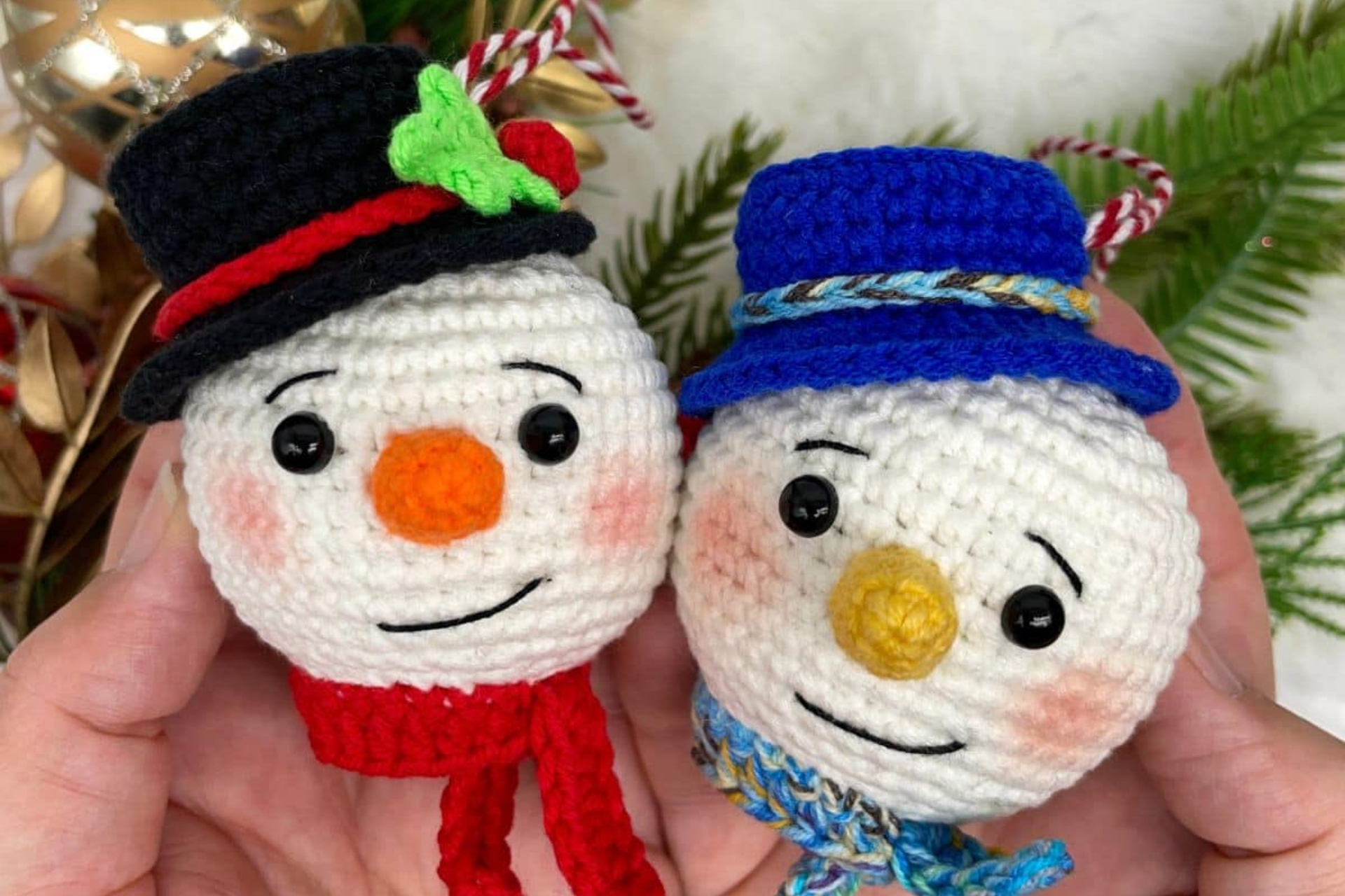 Two crocheted Snowman Ornaments by Cuddly Stitches Craft are held in hands; one features a red hat and scarf, the other a blue hat and scarf.