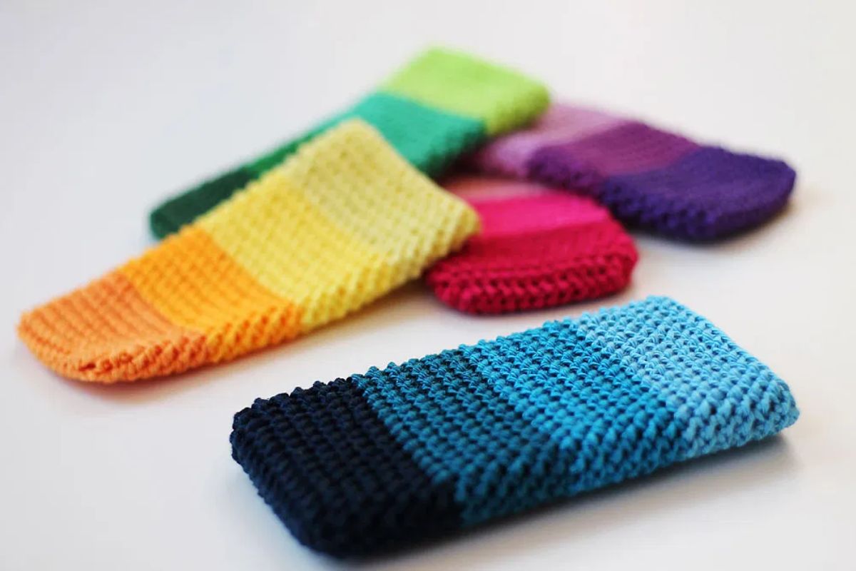 Four knitted or crocheted phone sleeves, including a charming Crocheted Snowman design, in gradient colors—blue, yellow-orange, green, and purple—lie on a white surface.