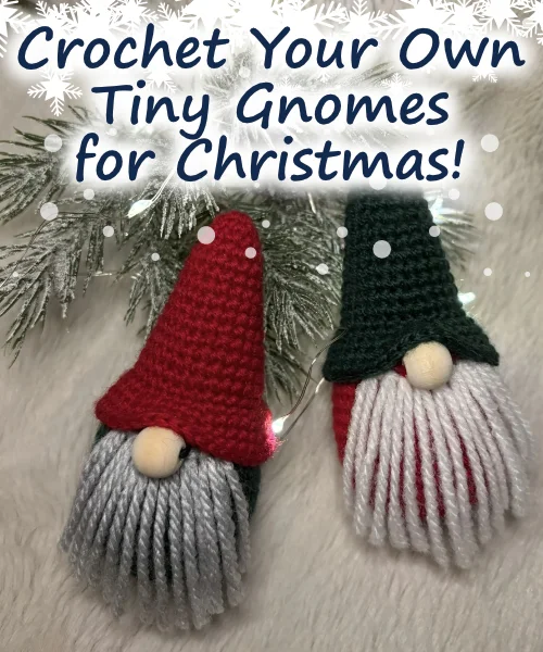 Two crocheted Christmas gnome ornaments with yarn beards and tall hats sit on a snowy surface beneath pine branches. Text reads: “Crochet Your Own Tiny Gnomes for Christmas with this Free Crochet Pattern!”.