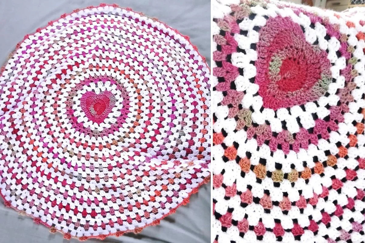 A round crocheted Baby Blanket with a Happy Heart pattern in the center, featuring pink, white, red, and brown yarn. A close-up highlights the texture and details of the stitches.