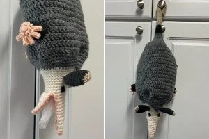 A crocheted opossum bag holder is hanging from a cabinet handle, with a plastic bag visible in its open mouth—perfect for animal lovers who also adore quirky Pop-up Animal Coasters.